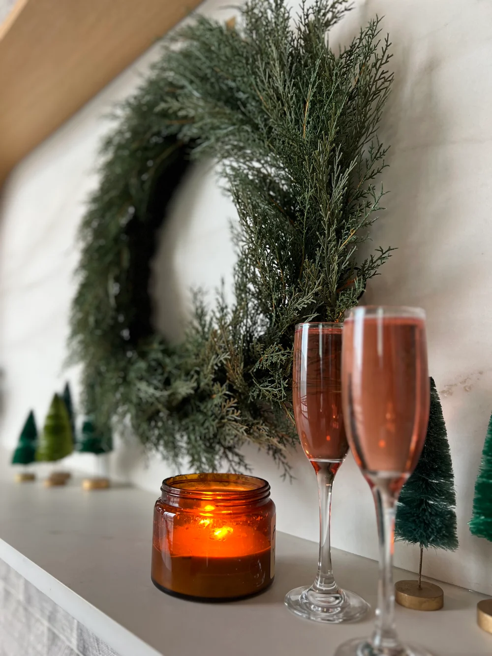 Holiday wreath hanging on a marble backdrop with a candle and pink champagne next to it at PINE Charlotte.