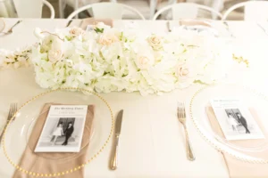 Wedding reception table with white tablecloths and white florals and gold accents